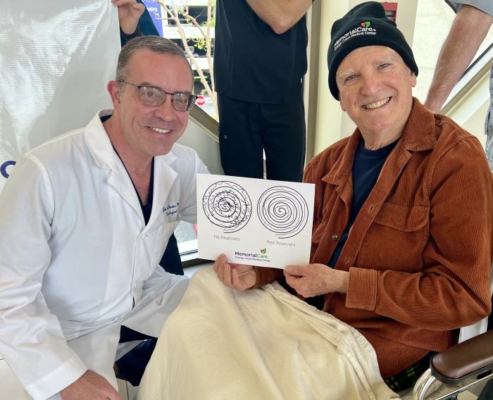 A doctor in a lab coat and a patient in a brown corduroy jacket hold a hand steadiness test. 