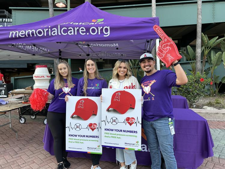 Four MemorialCare employees in branded gear standing in the front on Angels stadium with signs encouraging attendees to "know your numbers" for heart health.