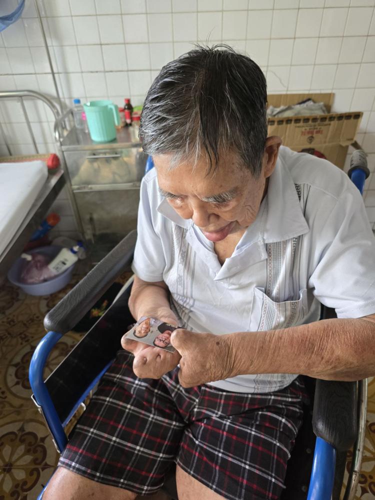 A man with leprosy sitting in a wheelchair gets emotional while looking at an old picture of himself. 