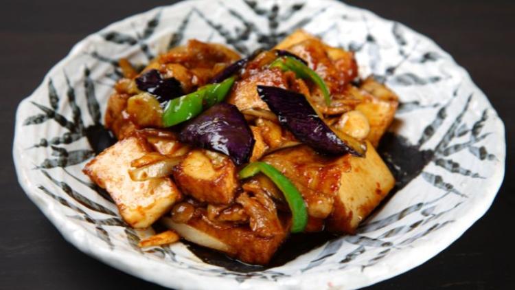 a bowl of eggplant stir fry served in a white bowl with black trees painted on it