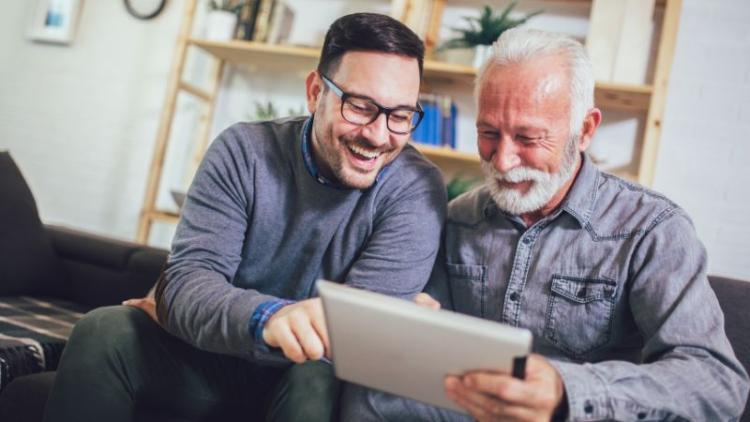 Two men sitting on a couch looking at a tablet.