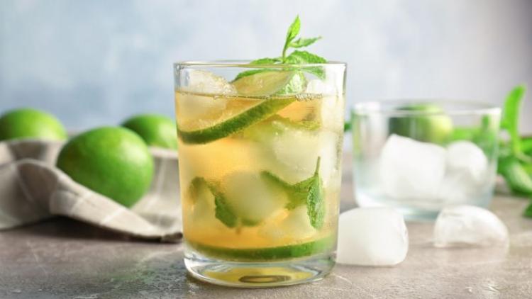 Mint julep mocktail surrounded by fresh lime, mint and ice on a marble table.