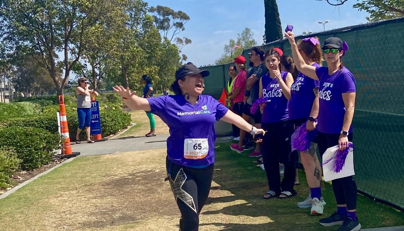A woman in a purple t-shirt running through a park on the grass.