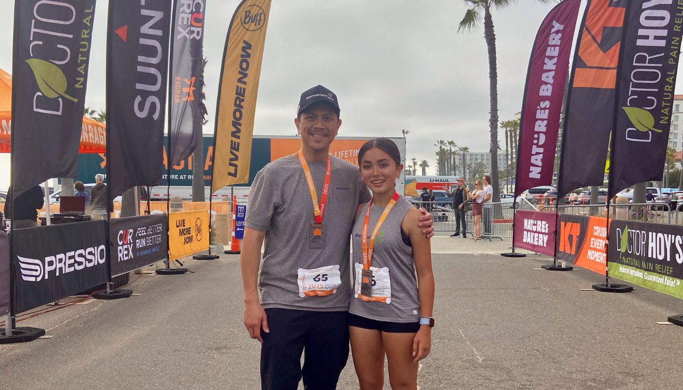 A man and young woman stand side by side at the finish line of a running race. 
